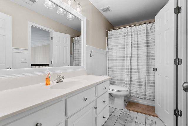 full bathroom with marble finish floor, a wainscoted wall, visible vents, toilet, and vanity