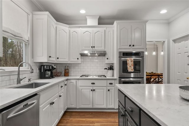 kitchen with stainless steel appliances, ornamental molding, white cabinets, a sink, and under cabinet range hood