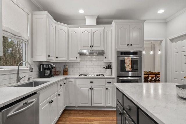 kitchen featuring white cabinets, appliances with stainless steel finishes, crown molding, under cabinet range hood, and a sink