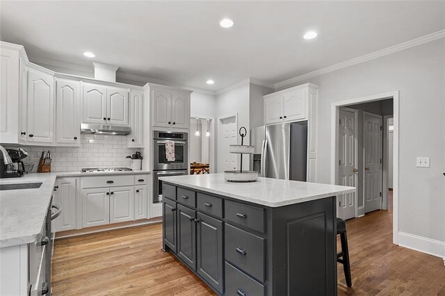 kitchen featuring decorative backsplash, appliances with stainless steel finishes, white cabinets, light hardwood / wood-style floors, and a kitchen island