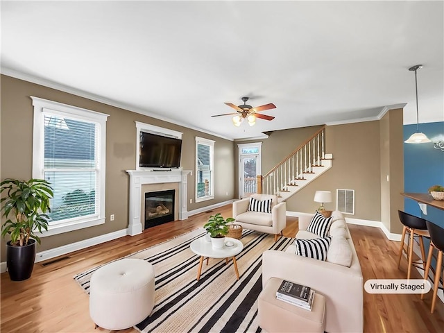 living area with baseboards, wood finished floors, a glass covered fireplace, and crown molding