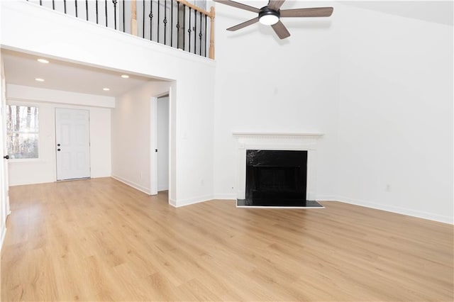 unfurnished living room featuring ceiling fan, a towering ceiling, and light hardwood / wood-style floors