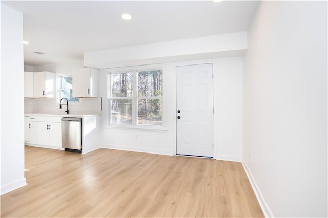 kitchen featuring white cabinets, dishwasher, decorative backsplash, sink, and light wood-type flooring