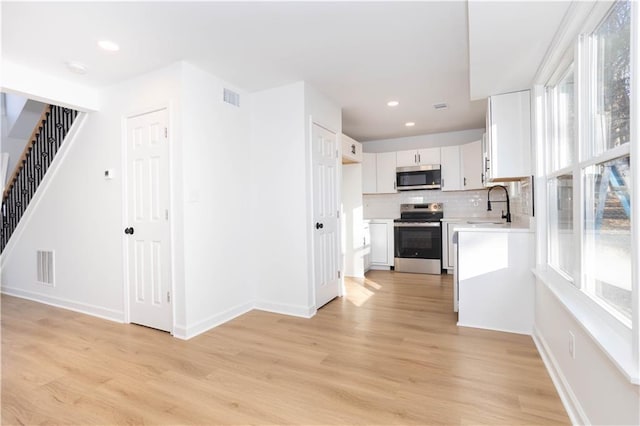 kitchen with decorative backsplash, sink, white cabinetry, light hardwood / wood-style flooring, and stainless steel appliances