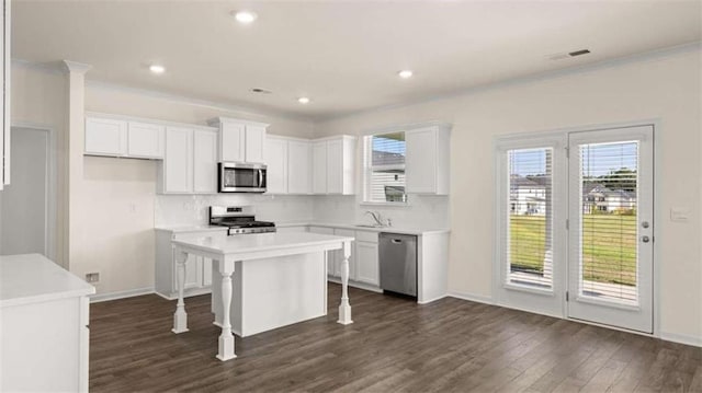 kitchen with dark wood-type flooring, a kitchen bar, white cabinetry, appliances with stainless steel finishes, and a kitchen island