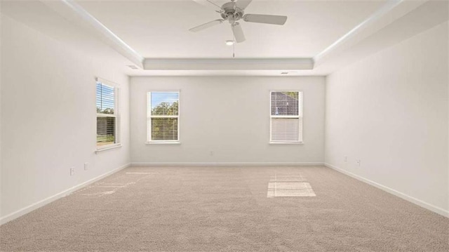 unfurnished room with a raised ceiling, light carpet, and ceiling fan