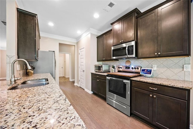 110 Collingwood Lndg, Covington, GA 30016 - kitchen featuring appliances with stainless steel finishes, crown molding, dark brown cabinets, light wood-style floors, and decorative backsplash