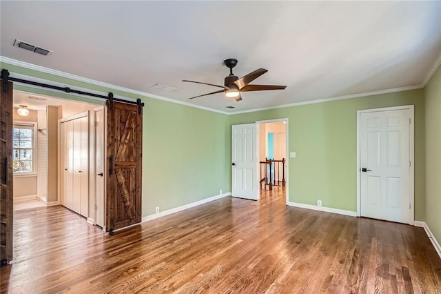 empty room featuring a barn door, ceiling fan, ornamental molding, and hardwood / wood-style flooring