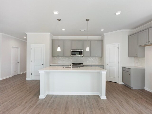 kitchen featuring gray cabinetry, a kitchen island with sink, pendant lighting, light wood-type flooring, and ornamental molding