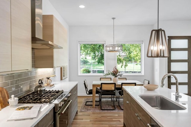 kitchen with pendant lighting, appliances with stainless steel finishes, sink, and wall chimney range hood