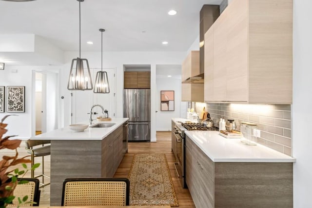 kitchen with sink, tasteful backsplash, decorative light fixtures, appliances with stainless steel finishes, and light hardwood / wood-style floors