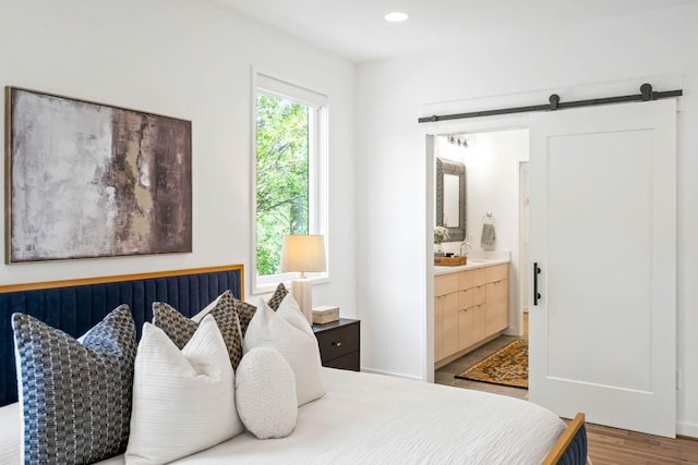 bedroom with sink, wood-type flooring, a barn door, and ensuite bathroom