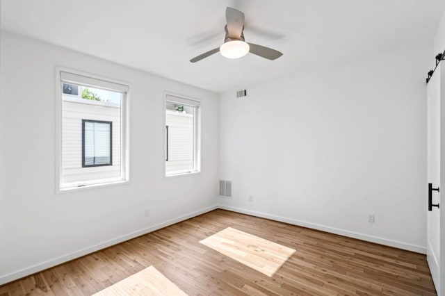 empty room featuring ceiling fan, wood-type flooring, and a barn door