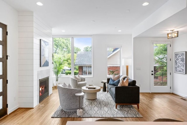 living room featuring plenty of natural light, a tiled fireplace, and light hardwood / wood-style floors