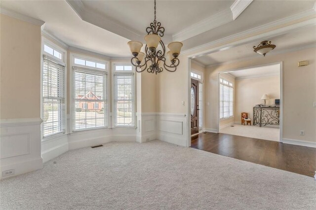 empty room with a raised ceiling, stairway, an inviting chandelier, ornamental molding, and wainscoting