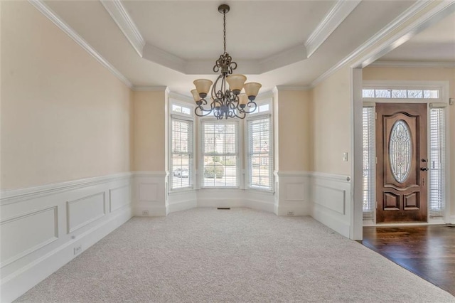 carpeted foyer entrance featuring an inviting chandelier, a tray ceiling, a decorative wall, and crown molding