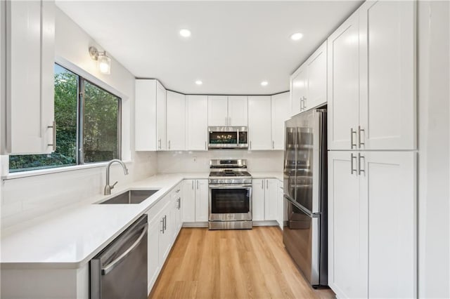 kitchen with white cabinetry, stainless steel appliances, sink, and light wood-type flooring