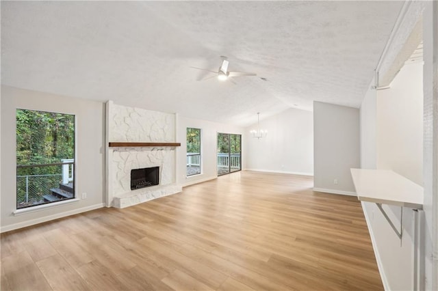 unfurnished living room with light wood-type flooring, ceiling fan with notable chandelier, a fireplace, a textured ceiling, and vaulted ceiling