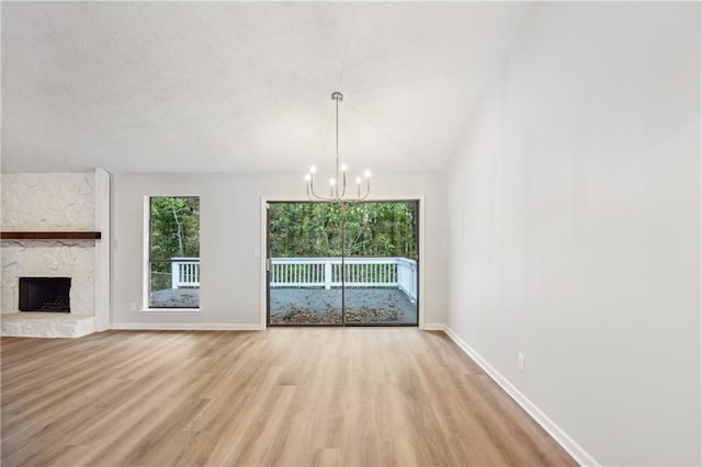 unfurnished living room with lofted ceiling, a stone fireplace, a notable chandelier, light wood-type flooring, and a textured ceiling