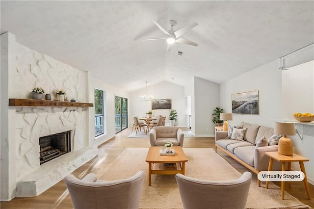 living room featuring light hardwood / wood-style flooring, lofted ceiling, ceiling fan with notable chandelier, and a fireplace