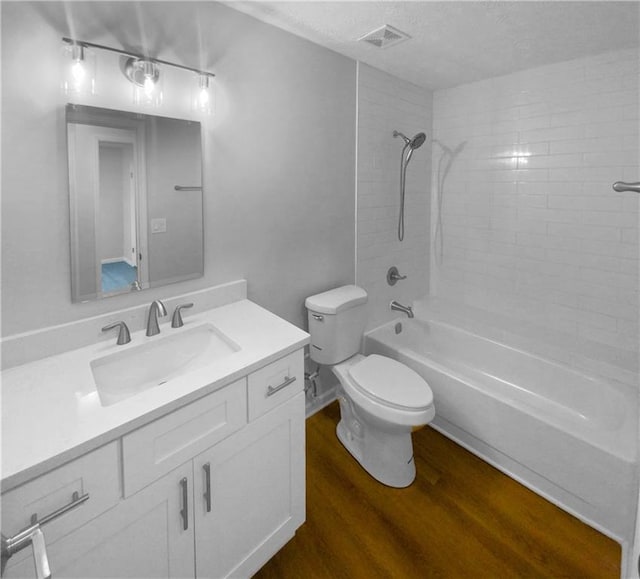 full bathroom featuring a textured ceiling, toilet, tiled shower / bath, vanity, and hardwood / wood-style flooring