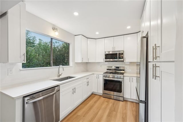 kitchen with decorative backsplash, white cabinetry, light hardwood / wood-style flooring, sink, and stainless steel appliances