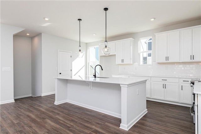 kitchen with a sink, a kitchen island with sink, dark wood-type flooring, backsplash, and baseboards