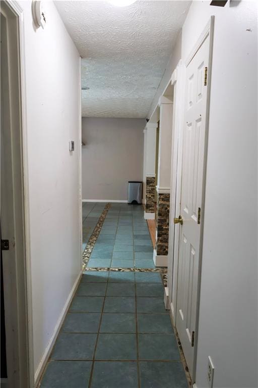 hallway with a textured ceiling and dark tile patterned flooring