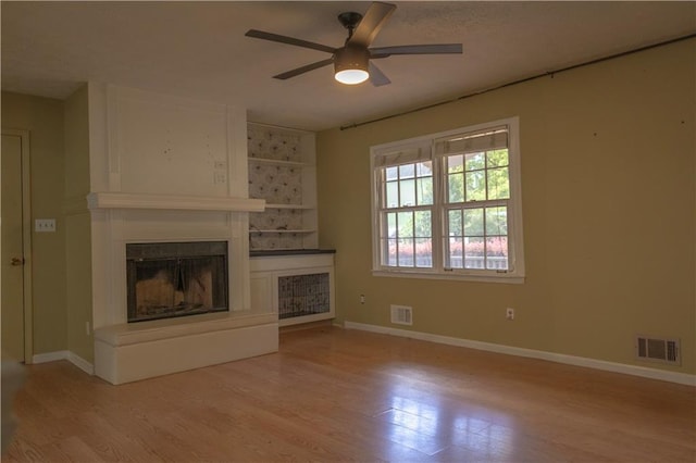 unfurnished living room featuring ceiling fan, a fireplace, and light wood-type flooring