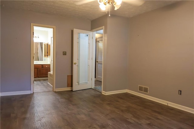 unfurnished bedroom with a textured ceiling, ensuite bath, dark wood-type flooring, and ceiling fan