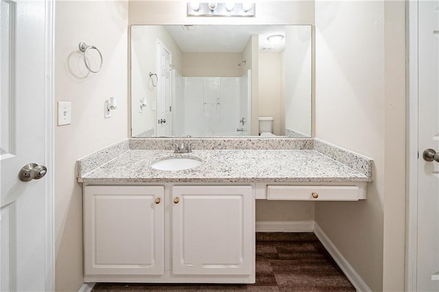 full bath with toilet, vanity, baseboards, and walk in shower