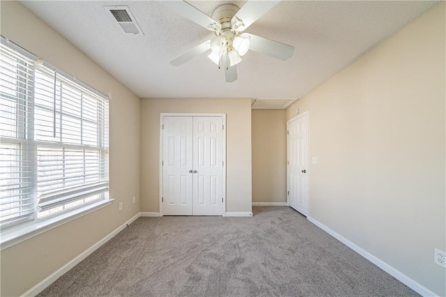 unfurnished bedroom featuring carpet, a closet, visible vents, a textured ceiling, and baseboards