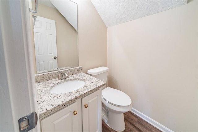 half bath with toilet, a textured ceiling, vanity, wood finished floors, and baseboards