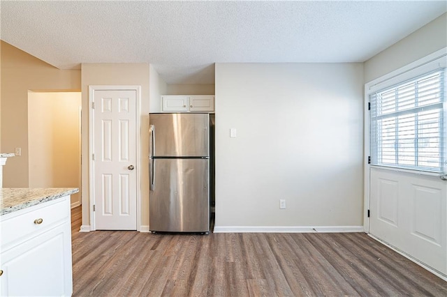 kitchen with light stone countertops, white cabinets, wood finished floors, and freestanding refrigerator