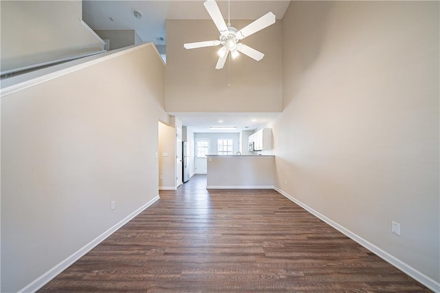 unfurnished living room with dark wood-type flooring, a high ceiling, baseboards, and a ceiling fan