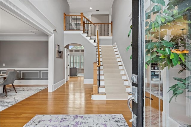 foyer featuring arched walkways, wood finished floors, baseboards, stairs, and crown molding