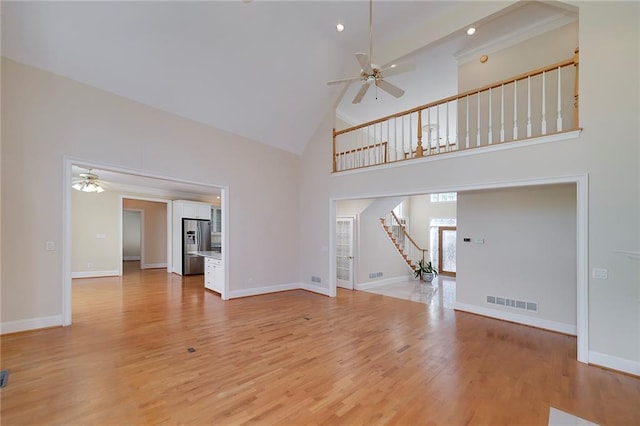 unfurnished living room featuring stairway, visible vents, a ceiling fan, light wood-style flooring, and high vaulted ceiling