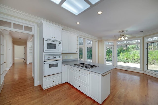 kitchen with a peninsula, light wood-type flooring, a wealth of natural light, and white appliances