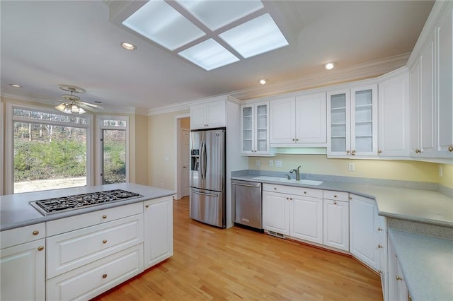 kitchen featuring crown molding, a sink, glass insert cabinets, stainless steel appliances, and light countertops