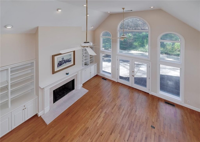 unfurnished living room featuring a fireplace with flush hearth, vaulted ceiling, visible vents, and light wood finished floors