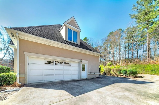view of side of property with concrete driveway, stucco siding, a shingled roof, and a garage