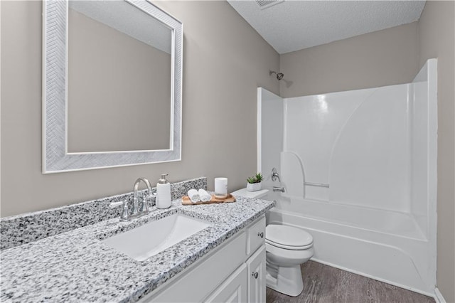 full bathroom featuring toilet, shower / tub combination, vanity, wood finished floors, and a textured ceiling