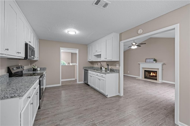 kitchen featuring stainless steel appliances, a ceiling fan, white cabinets, light wood-style floors, and baseboards