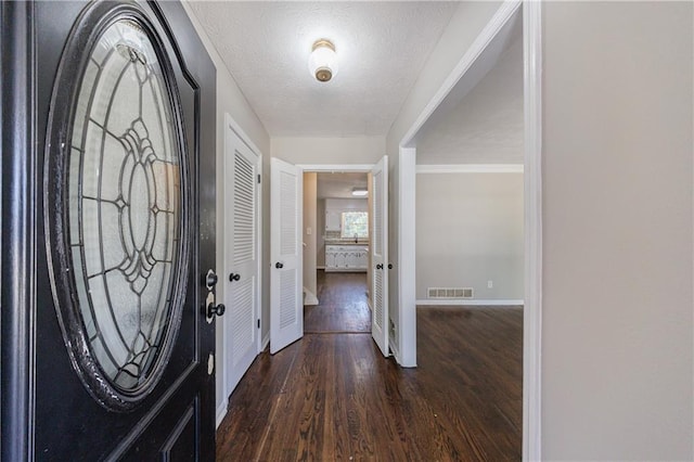 foyer entrance featuring visible vents, baseboards, a textured ceiling, and wood finished floors