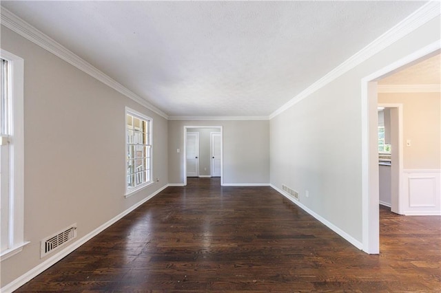 empty room with a wealth of natural light, visible vents, ornamental molding, and wood finished floors