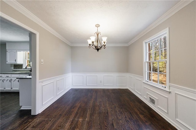 unfurnished dining area featuring visible vents, a wainscoted wall, dark wood-type flooring, a textured ceiling, and a chandelier