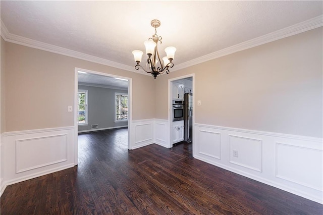 unfurnished dining area featuring dark wood finished floors, a wainscoted wall, crown molding, and an inviting chandelier