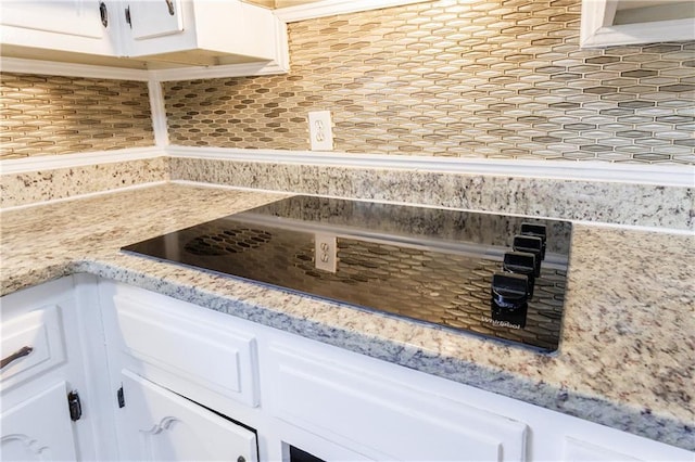 interior details featuring backsplash, white cabinetry, black electric cooktop, and light stone countertops