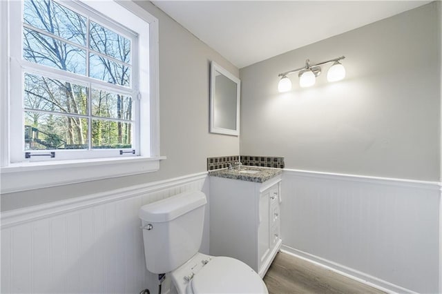 bathroom with vanity, toilet, wood finished floors, and wainscoting