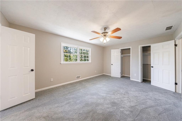 unfurnished bedroom featuring visible vents, a textured ceiling, multiple closets, and carpet floors